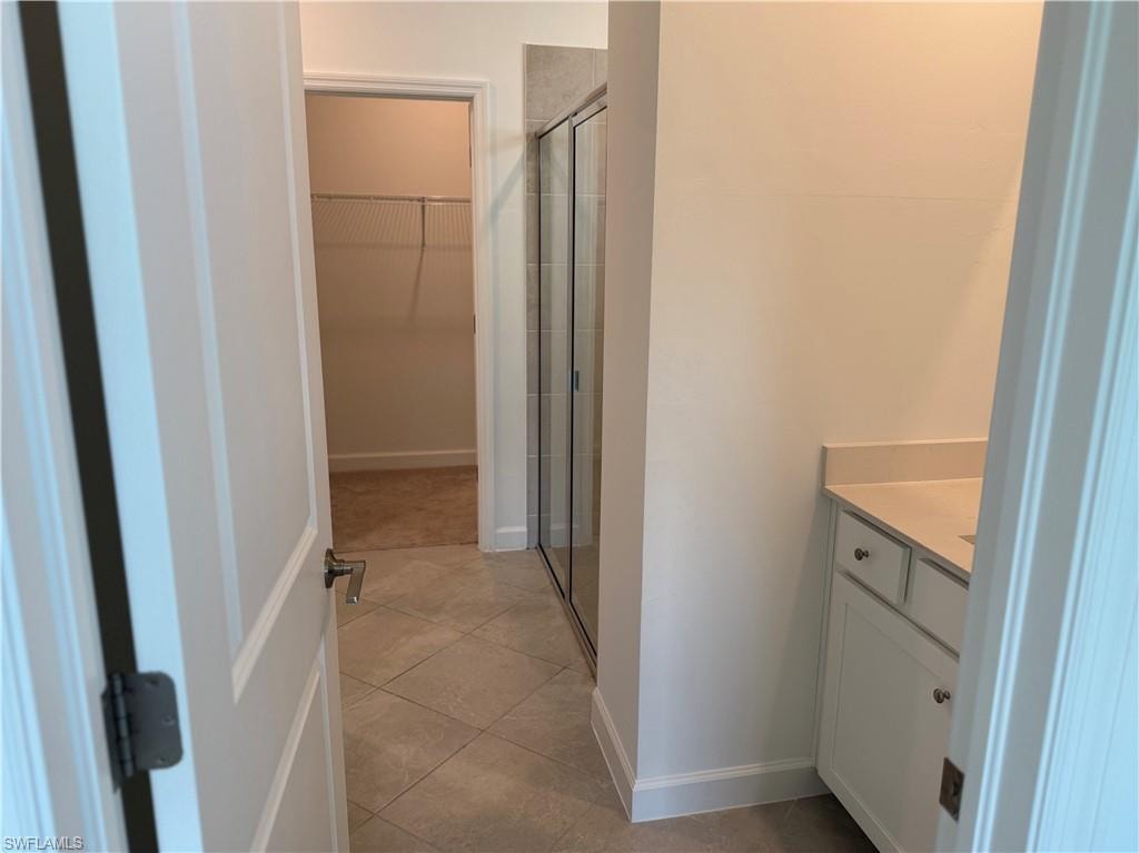 Bathroom featuring a glass-enclosed shower, single vanity with light-colored countertop, white cabinetry with silver hardware, and diagonally-laid floor tiles