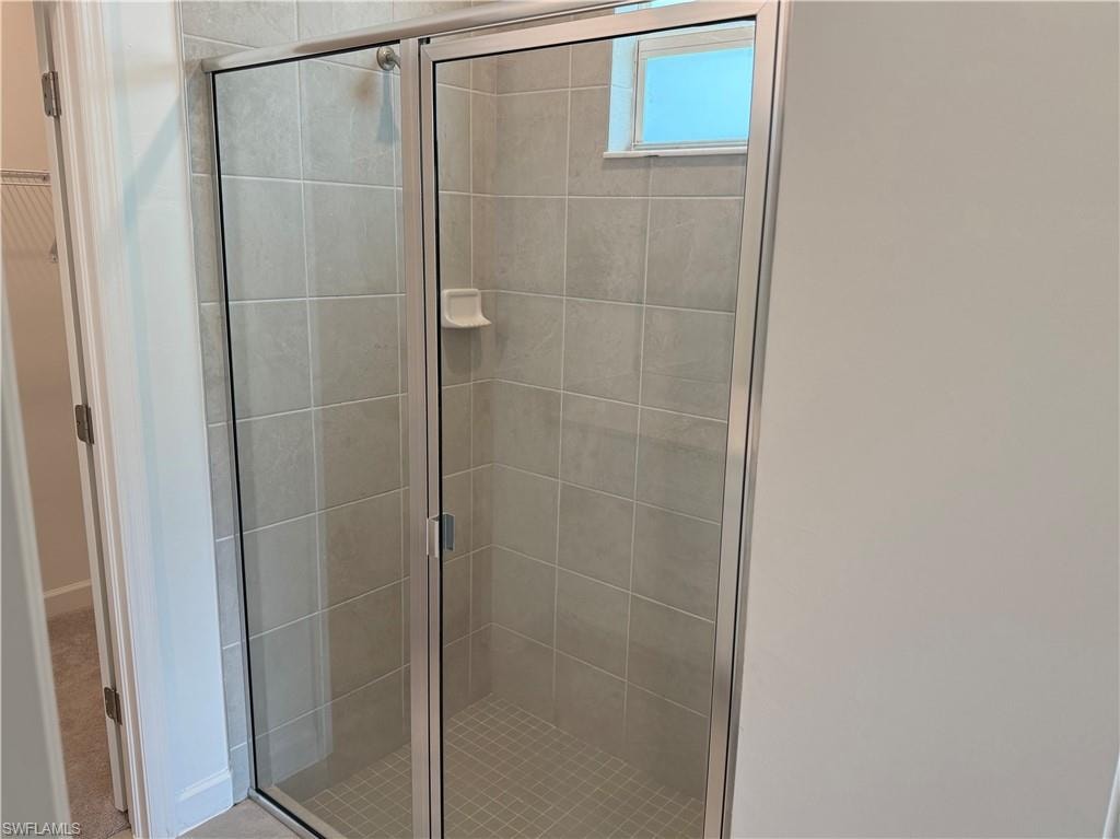 Walk-in shower featuring light-toned tile, a glass enclosure with a silver-tone frame, and a small window for natural light