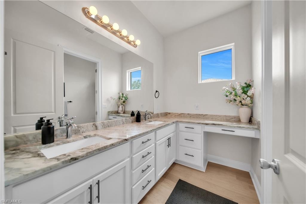 (Guest Bathroom) Spacious bathroom featuring a dual vanity with light-toned stone countertops, white shaker cabinetry, and wood-finish flooring