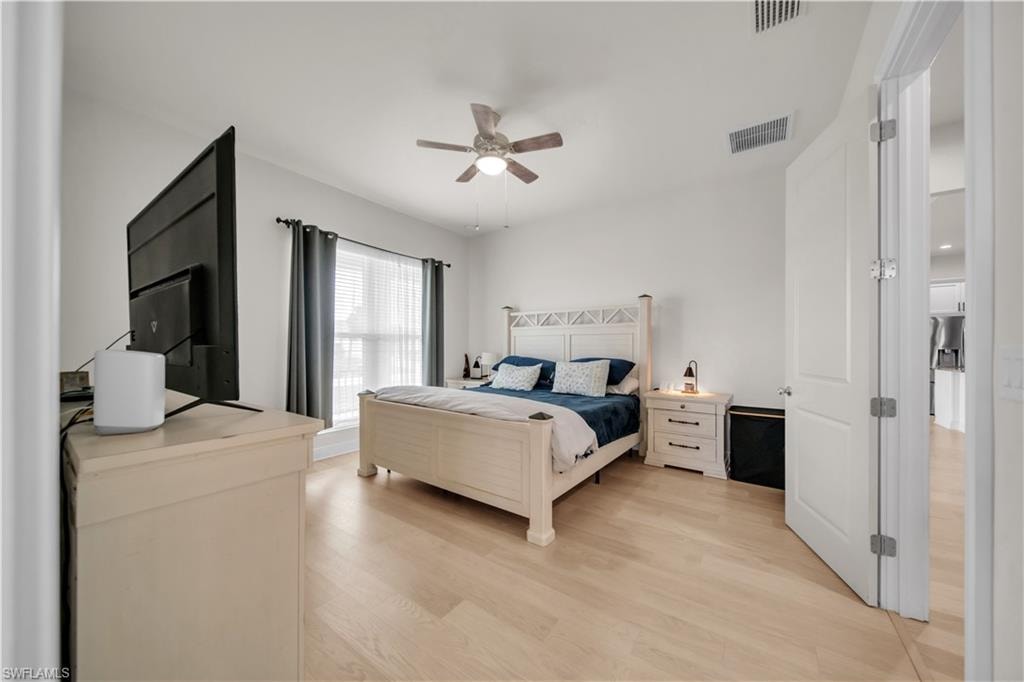 (Master Bedroom)Spacious bedroom featuring light wood-finish flooring, a ceiling fan with integrated lighting, and a large window with privacy blinds