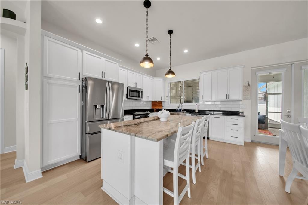 Modern kitchen featuring a large central island with seating, stainless steel appliances, white cabinetry, and light wood-finish flooring