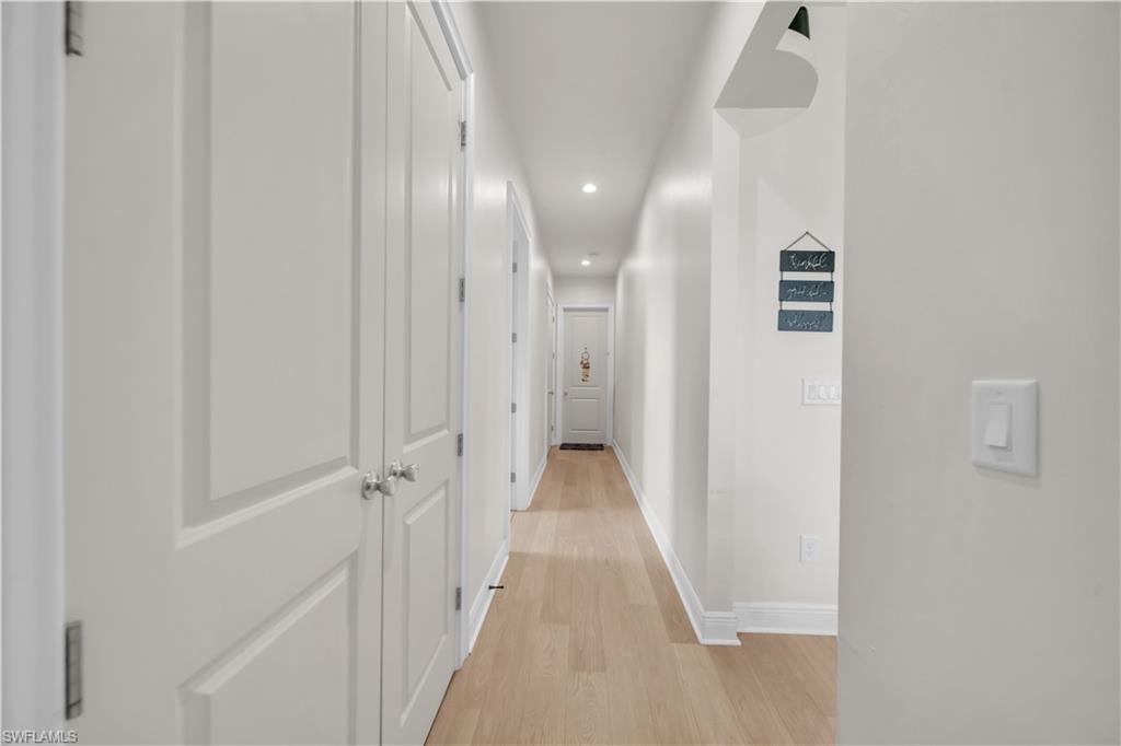 Bright hallway featuring light wood-finish flooring, recessed lighting, white panel doors, and contrasting baseboards