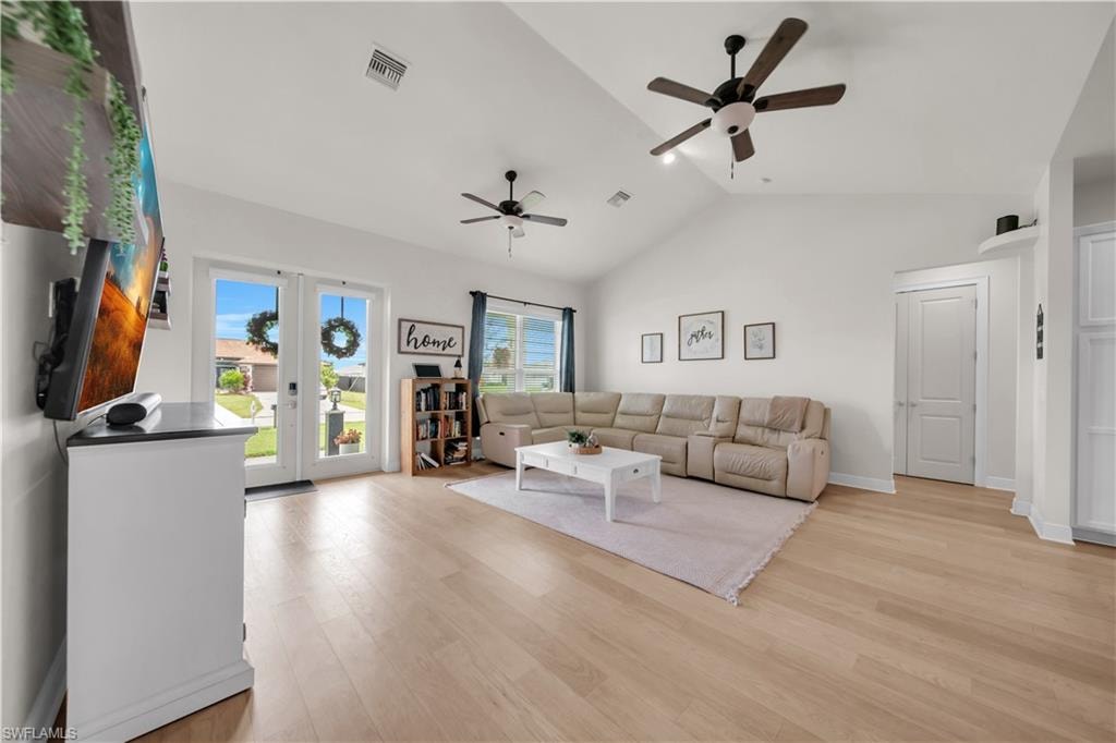 Spacious living area featuring light wood-finish flooring, vaulted ceilings, and two ceiling fans