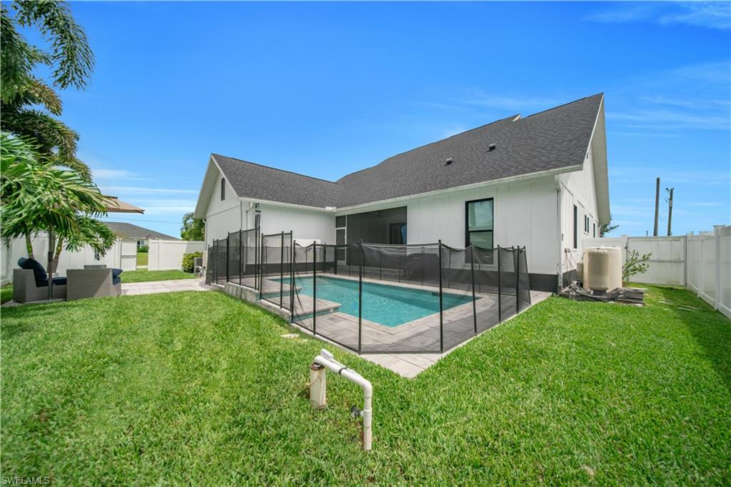 Rear exterior featuring a fenced swimming pool, expansive lawn, and white privacy fencing