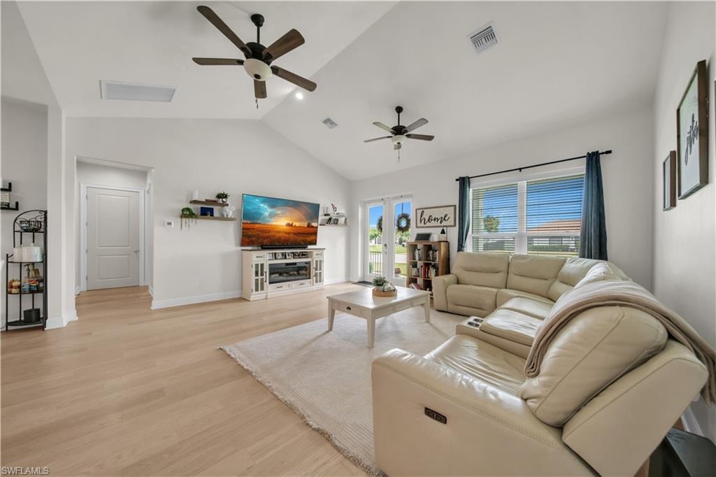 Bright living area featuring vaulted ceilings, light wood-finish flooring, multiple ceiling fans, recessed lighting, and white baseboards