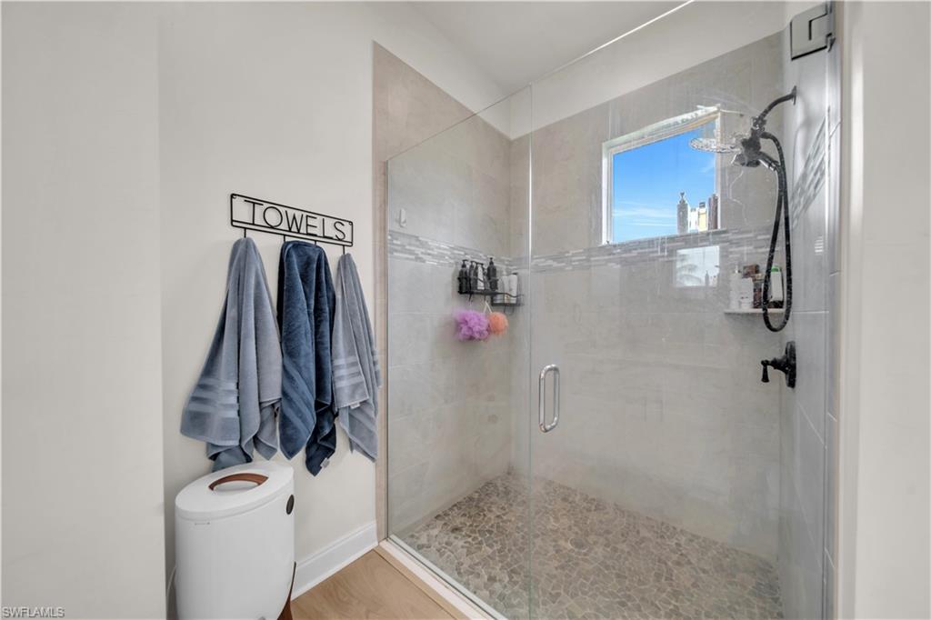 Walk-in shower featuring a frameless glass enclosure, pebble tile floor, light gray subway tile walls, a horizontal mosaic accent band, and a window