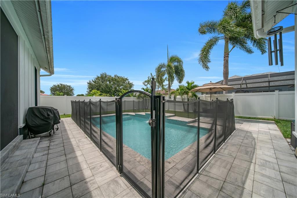 Private outdoor area featuring a swimming pool with a safety fence, paver patio, and white privacy fencing