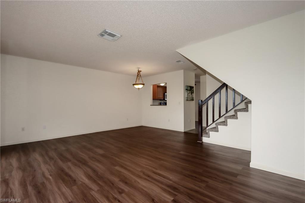 Unfurnished living room with dark wood-style flooring, stairs, and a textured ceiling