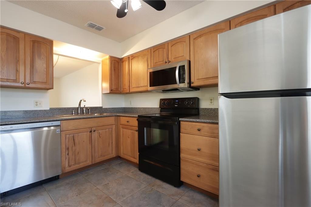 Kitchen featuring stainless steel appliances, dark countertops, a ceiling fan, and brown cabinets