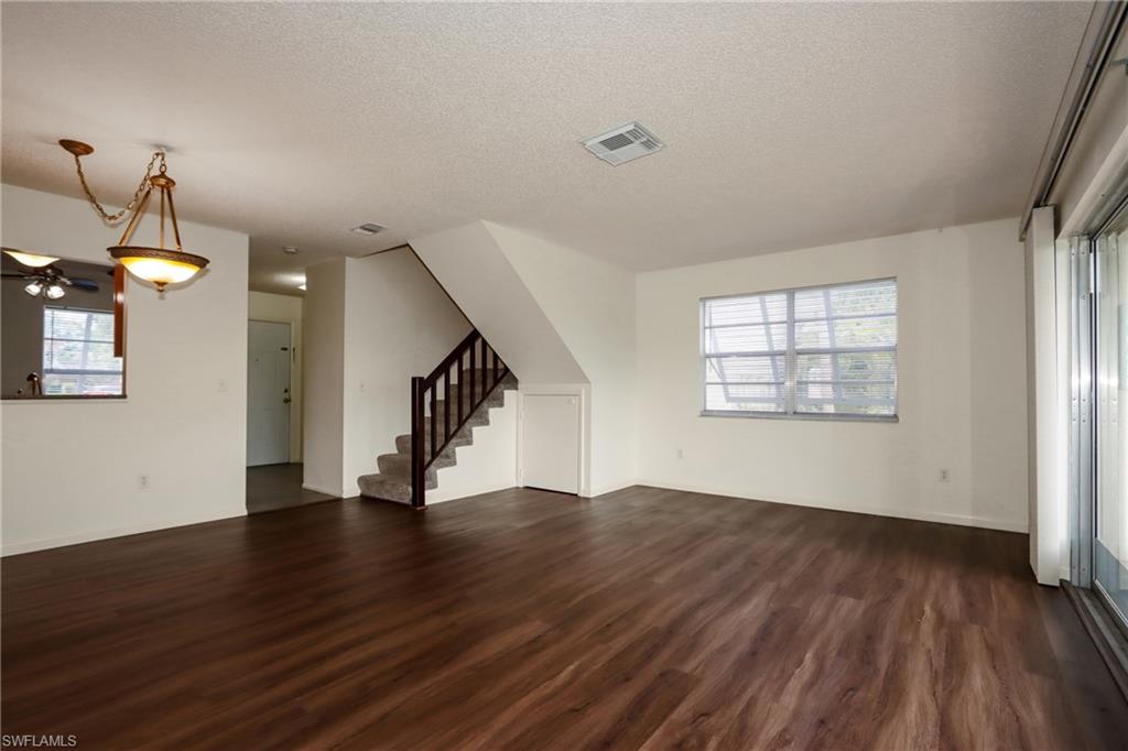 Unfurnished living room with a textured ceiling, dark wood-type flooring, stairs, and a ceiling fan