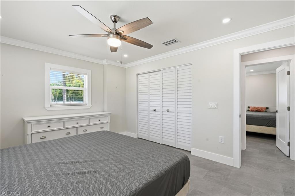 Interior room featuring light gray walls, crown molding, a window with horizontal blinds, wood-finish ceiling fan, and louvered bi-fold closet doors