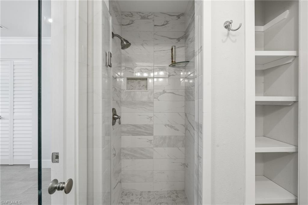 Walk-in shower featuring marble-patterned tile walls, a built-in shower niche, and a mosaic tile floor