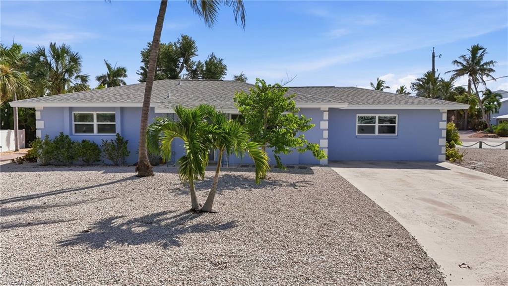 Single-story residence featuring a light blue exterior, white trim, and a gray shingle roof with low maintenance gravel yard.