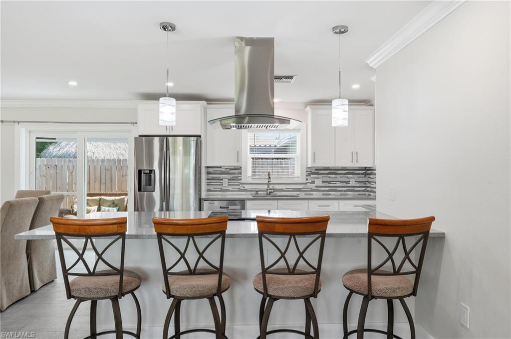 Contemporary kitchen featuring a large island with a light-toned quartz countertop, stainless steel appliances, white cabinetry, and a textured tile backsplash