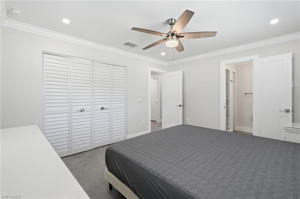 Spacious bedroom featuring light gray walls, crown molding, a ceiling fan with integrated lighting, recessed lighting, and large louvered bifold closet doors