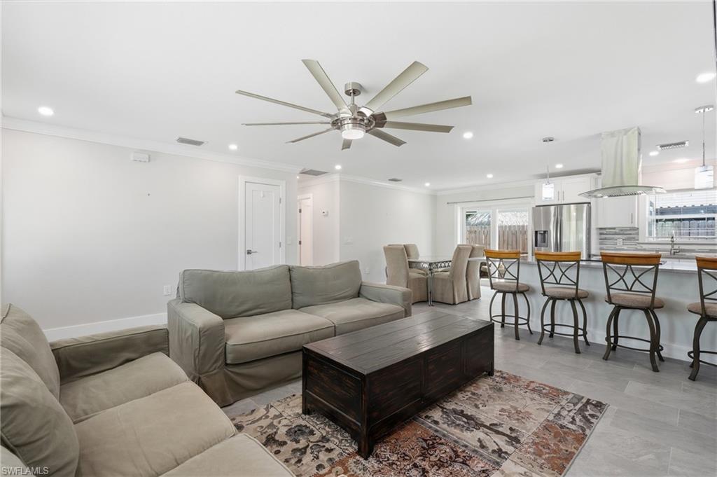 Open-concept living space featuring a modern ceiling fan, recessed lighting, crown molding, and wood-finish tile flooring