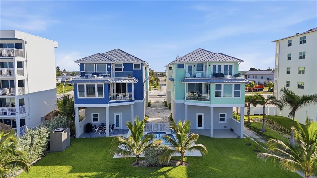 Two distinct homes featuring metal roofs, elevated foundations, multiple balconies, and a shared in-ground pool - Virtually Edited Image