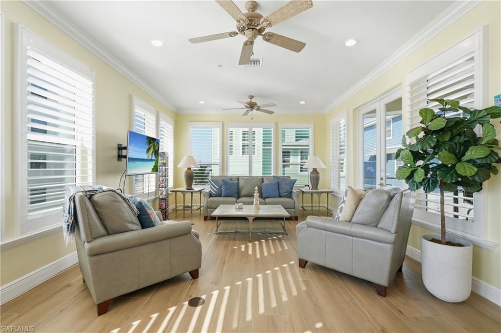 Expansive open-concept interior featuring light wood-finish flooring, white plantation shutters, and a ceiling fan with integrated lighting - Virtually Edited Image