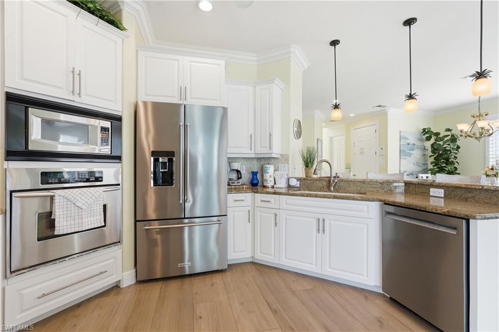 Kitchen featuring white cabinetry, stainless steel appliances, wood-finish flooring, and pendant lighting - Virtually Edited Image