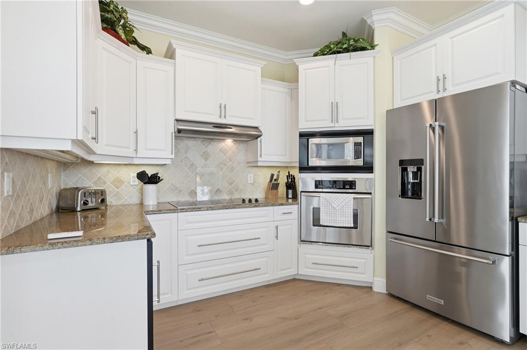 White cabinetry, stainless steel appliances, granite countertops, tile backsplash, and wood-finish flooring - Virtually Edited Image