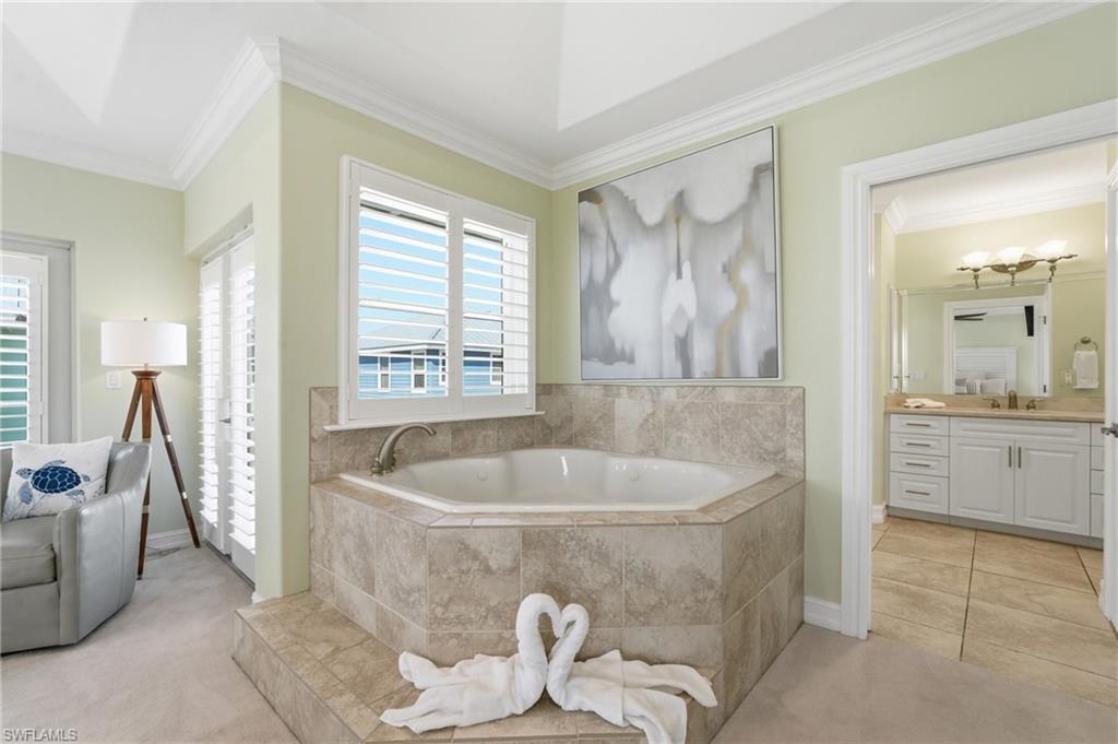 Built-in soaking tub with a tiled surround, plantation shutters, crown molding, and an attached bathroom with a double vanity - Virtually Edited Image