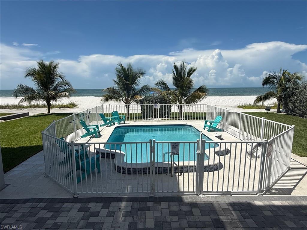 Fenced in-ground pool with integrated steps, surrounded by a paved patio and manicured lawn