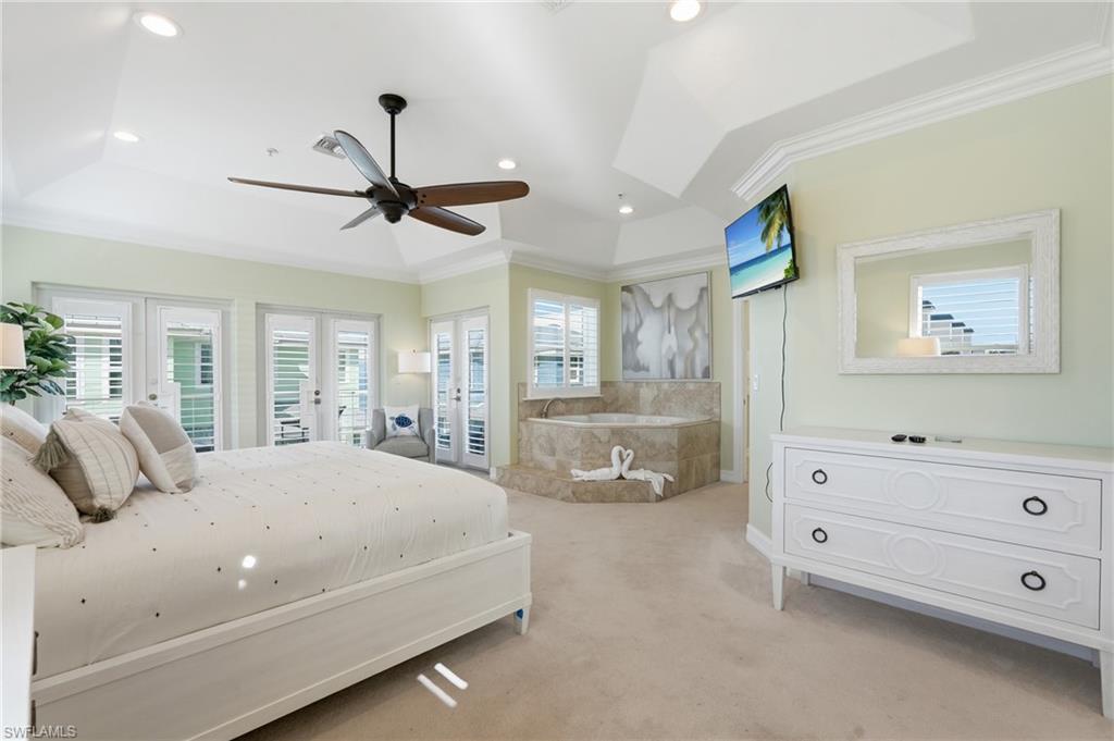 Tray ceiling featuring recessed lighting and a ceiling fan, multiple French doors with plantation shutters, built-in jetted tub with stone-look surround, and plush carpeting - Virtually Edited Image
