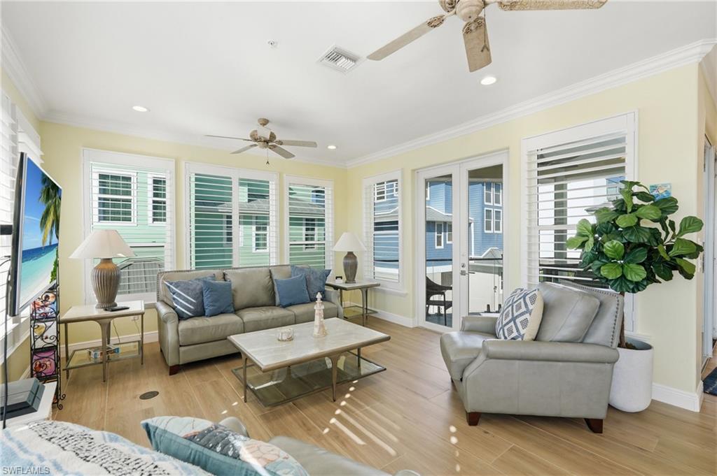 Expansive open-concept interior featuring light wood-finish flooring, white plantation shutters, and a ceiling fan with integrated lighting - Virtually Edited Image