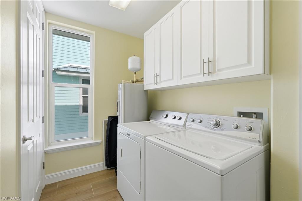 White shaker-style cabinetry, recessed ceiling light, wood-finish flooring, white paneled door, and a single-hung window - Virtually Edited Image