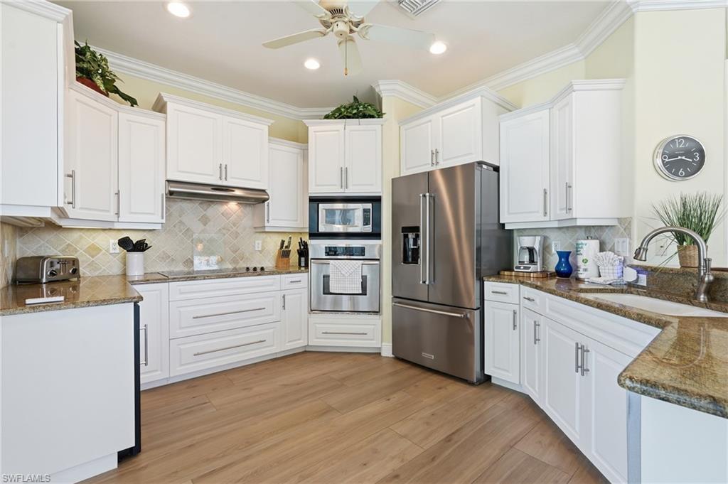 White cabinetry, stone countertops, stainless steel appliances, wood-finish flooring, and recessed lighting - Virtually Edited Image