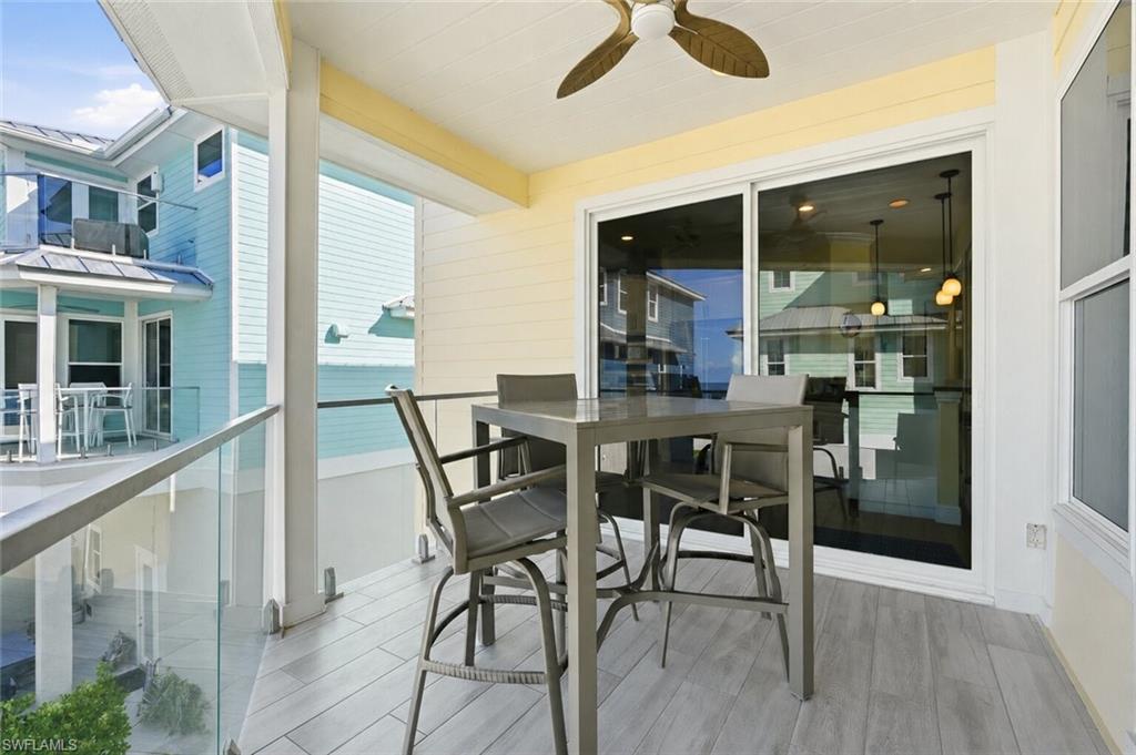 Covered balcony with wood-finish flooring, glass panel railing, and a ceiling fan - Virtually Edited Image
