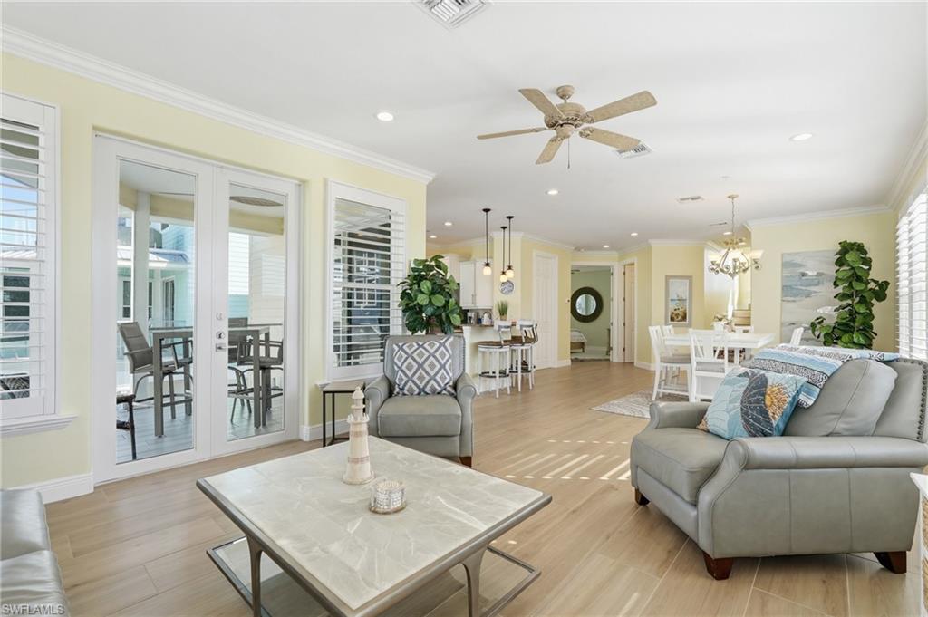 Expansive open-concept interior featuring light wood-finish flooring, white plantation shutters, and a ceiling fan with integrated lighting - Virtually Edited Image