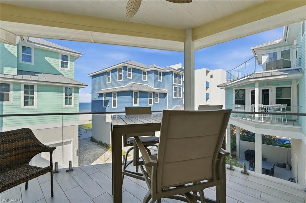 Covered balcony with wood-finish flooring, glass panel railing, and a ceiling fan - Virtually Edited Image