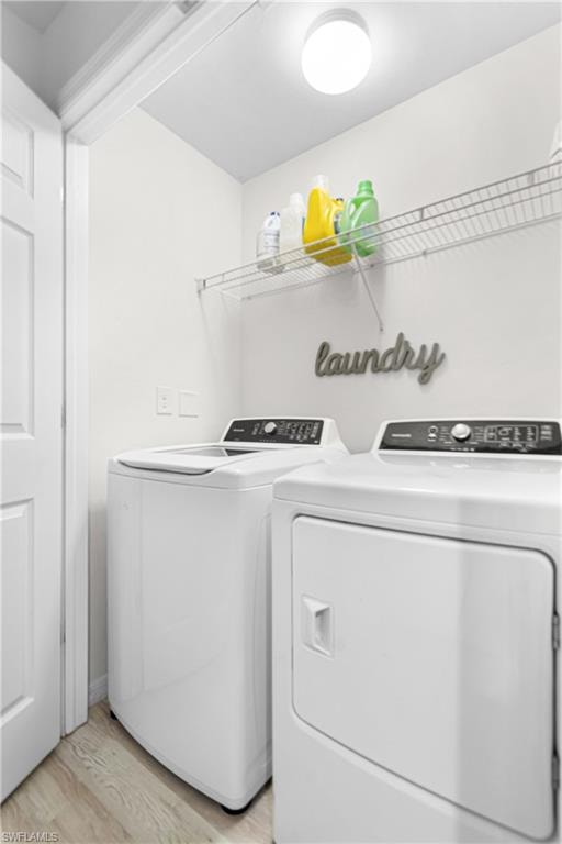 Dedicated laundry area featuring a washer and dryer set, overhead wire shelving, light wood-finish flooring, and a flush-mount ceiling light fixture