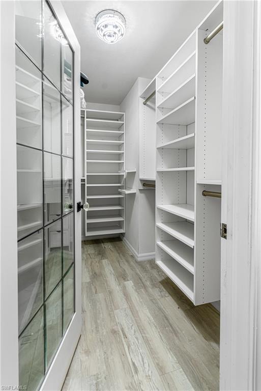 Walk-in closet featuring custom white built-in shelving, hanging rods, and wood-finish flooring