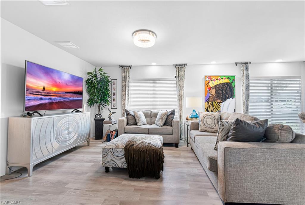 Spacious living area featuring wood-finish flooring, ample natural light from multiple windows with horizontal blinds, and recessed lighting with a central ceiling fixture