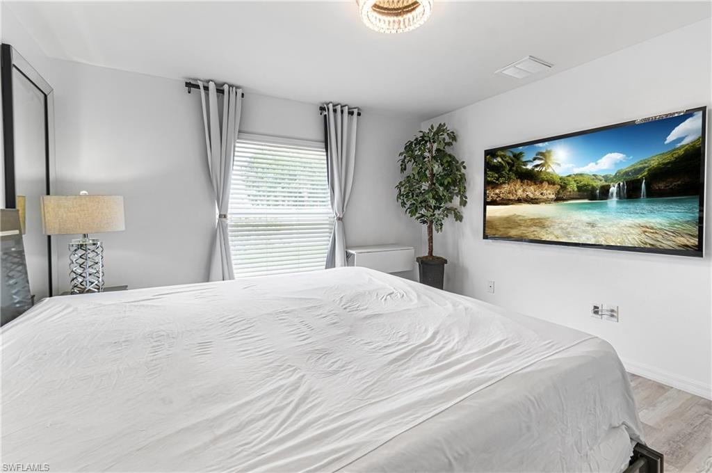 Bedroom featuring a wall-mounted television, wood-finish flooring, and a window with blinds