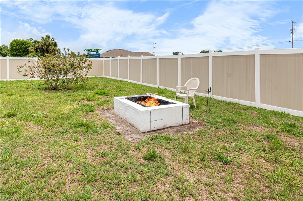 Expansive backyard featuring a concrete block fire pit, privacy fencing, and established shrubbery