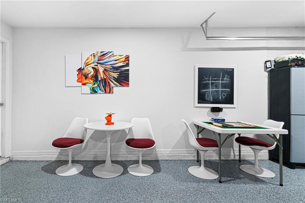Finished recreation room featuring light gray speckled flooring, white painted walls, and a built-in overhead track system