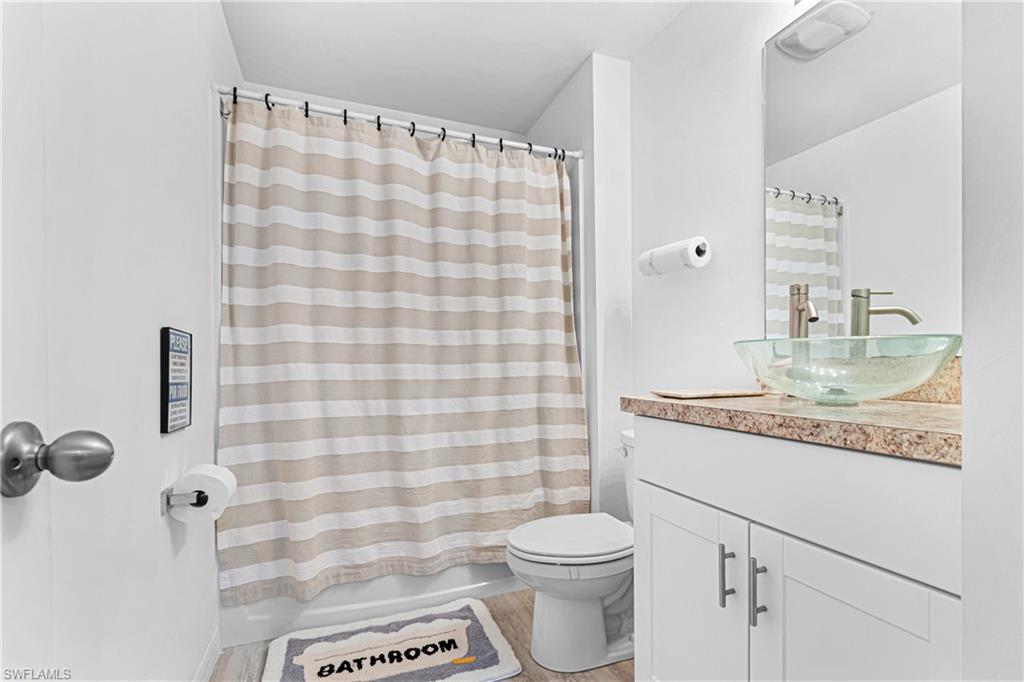 Bathroom featuring a glass vessel sink, white vanity with cabinet storage, a shower-tub combination, and light-toned wood-finish flooring