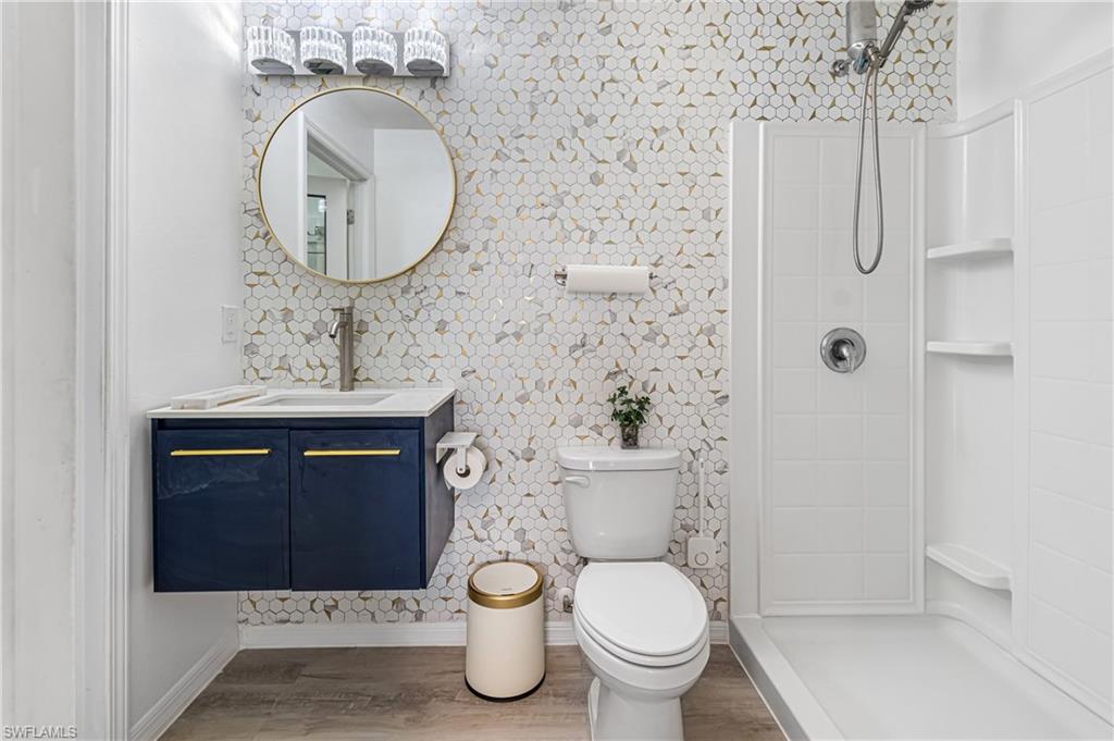 Renovated bathroom featuring a floating navy vanity with gold-tone hardware, a round frameless mirror, and a full wall of hexagonal mosaic tile