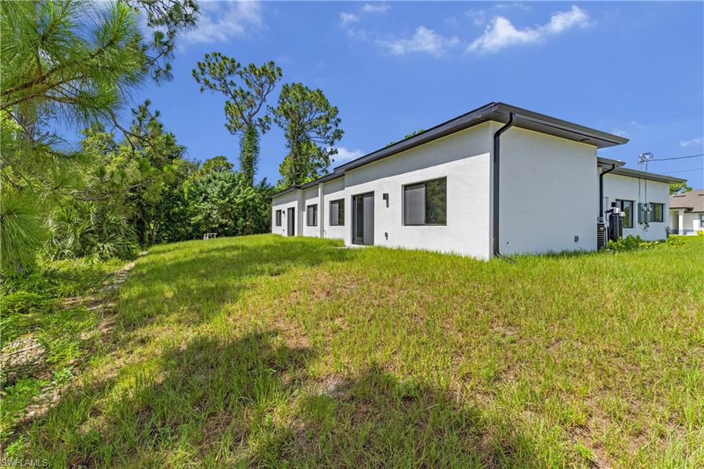 Modern stucco exterior with black-framed windows and a dark fascia, complemented by a large grassy area
