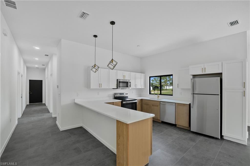 Modern kitchen featuring white shaker cabinetry, light wood-finish lower cabinets, stainless steel appliances, and a U-shaped countertop with a breakfast bar