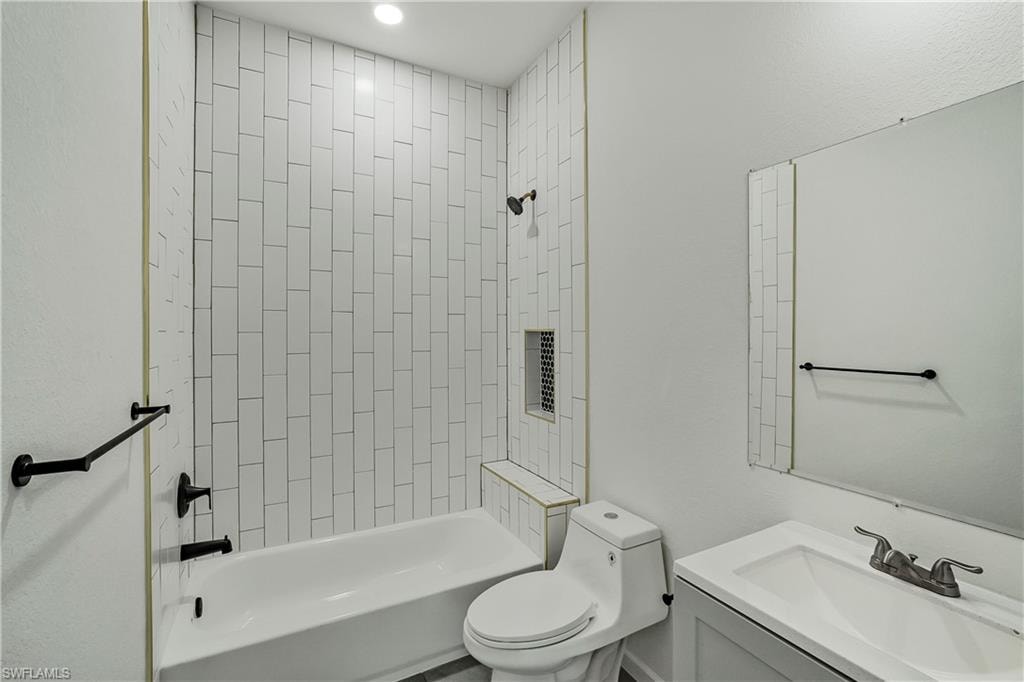 Bathroom featuring a white subway tile shower surround with a built-in niche, white bathtub, and matte black fixtures
