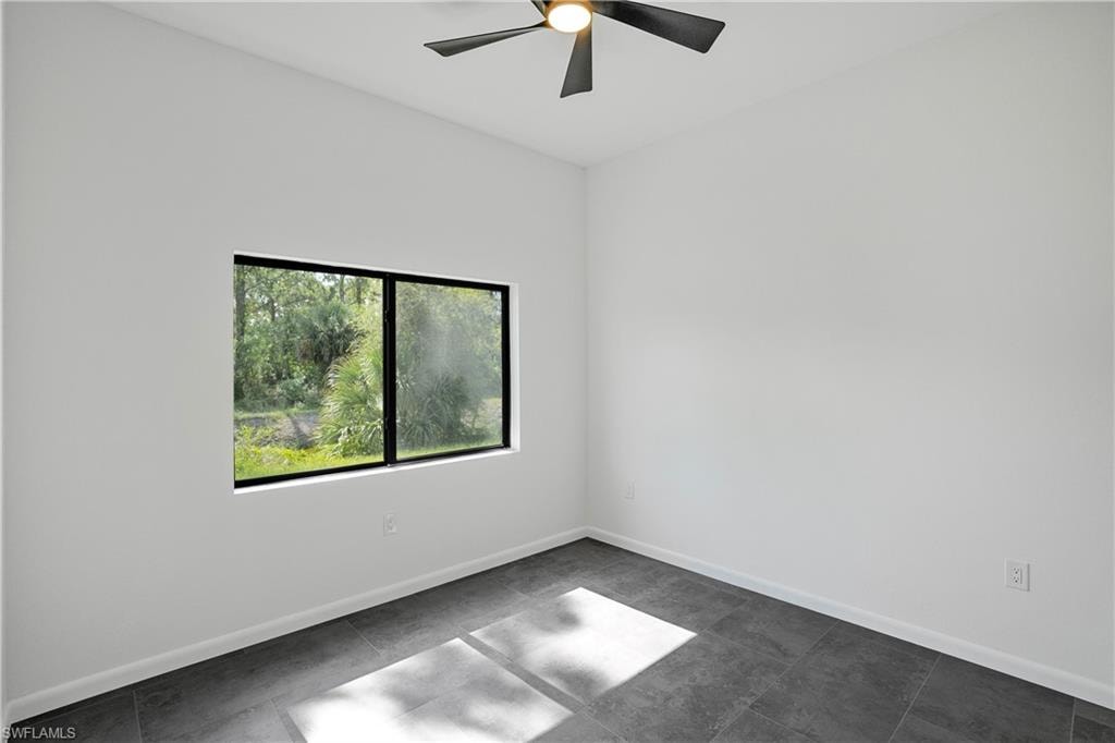 Room featuring a modern ceiling fan, large window with black trim, white walls, and dark gray tile flooring