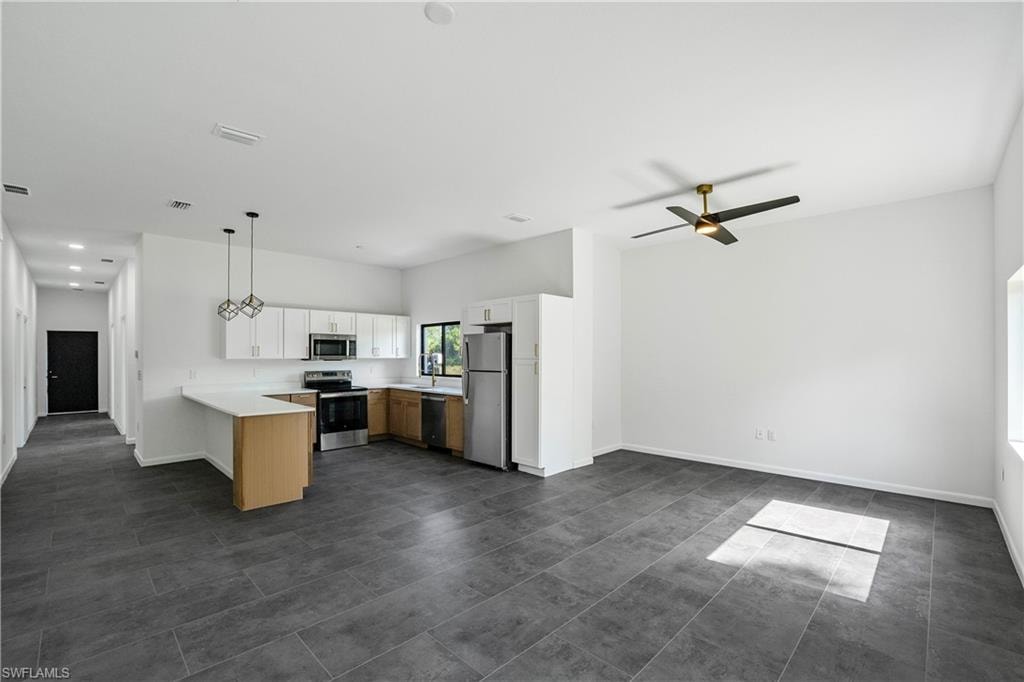 Open-concept living area featuring dark tile flooring, a contemporary ceiling fan, and a kitchen with light wood-finish cabinetry, stainless steel appliances, and a breakfast bar