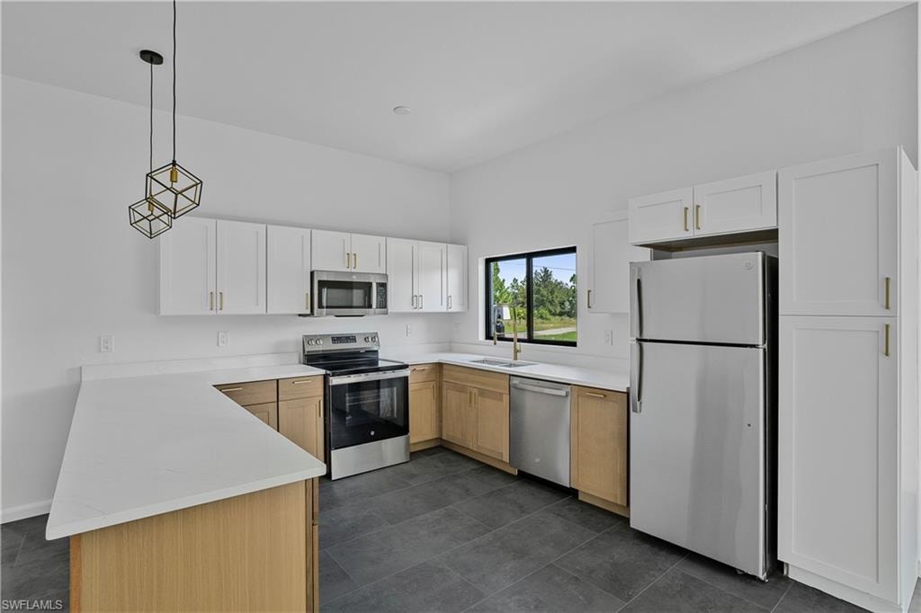 Modern kitchen featuring two-tone cabinetry, stainless steel appliances, white countertops, dark gray tile flooring, and a window above the sink