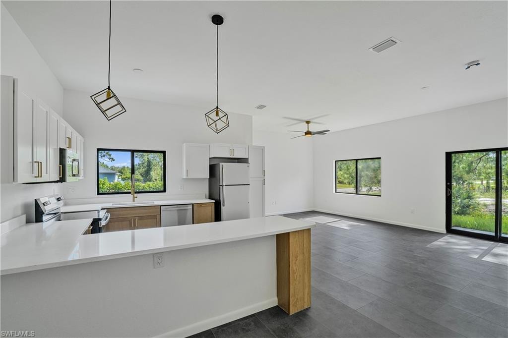 Open-concept living space featuring a modern kitchen with white cabinetry, light wood-finish lower cabinets, stainless steel appliances, and a breakfast bar