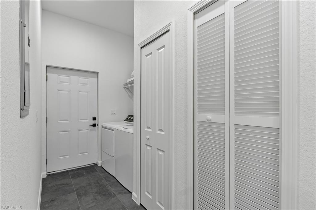 Laundry area featuring dark-toned floor tiling, a white paneled door, louvered bi-fold closet doors, and built-in shelving