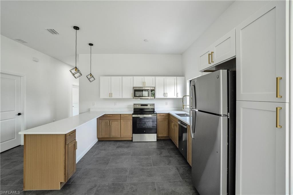 Kitchen featuring a peninsula island, two-tone cabinetry, stainless steel appliances, white countertops, and dark tile flooring